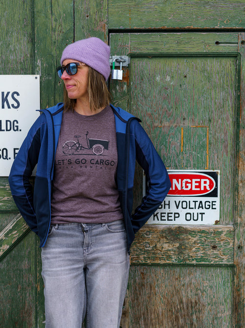 Person wearing a purple touque and sunglasses, standing in front of a wooden door with signs.