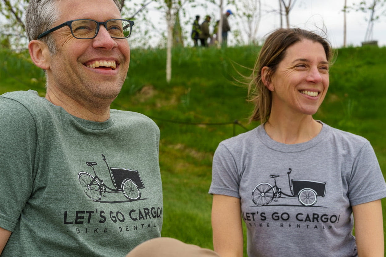 Two people wearing 'Let's Go Cargo' t-shirts sitting outdoors on a grassy area.