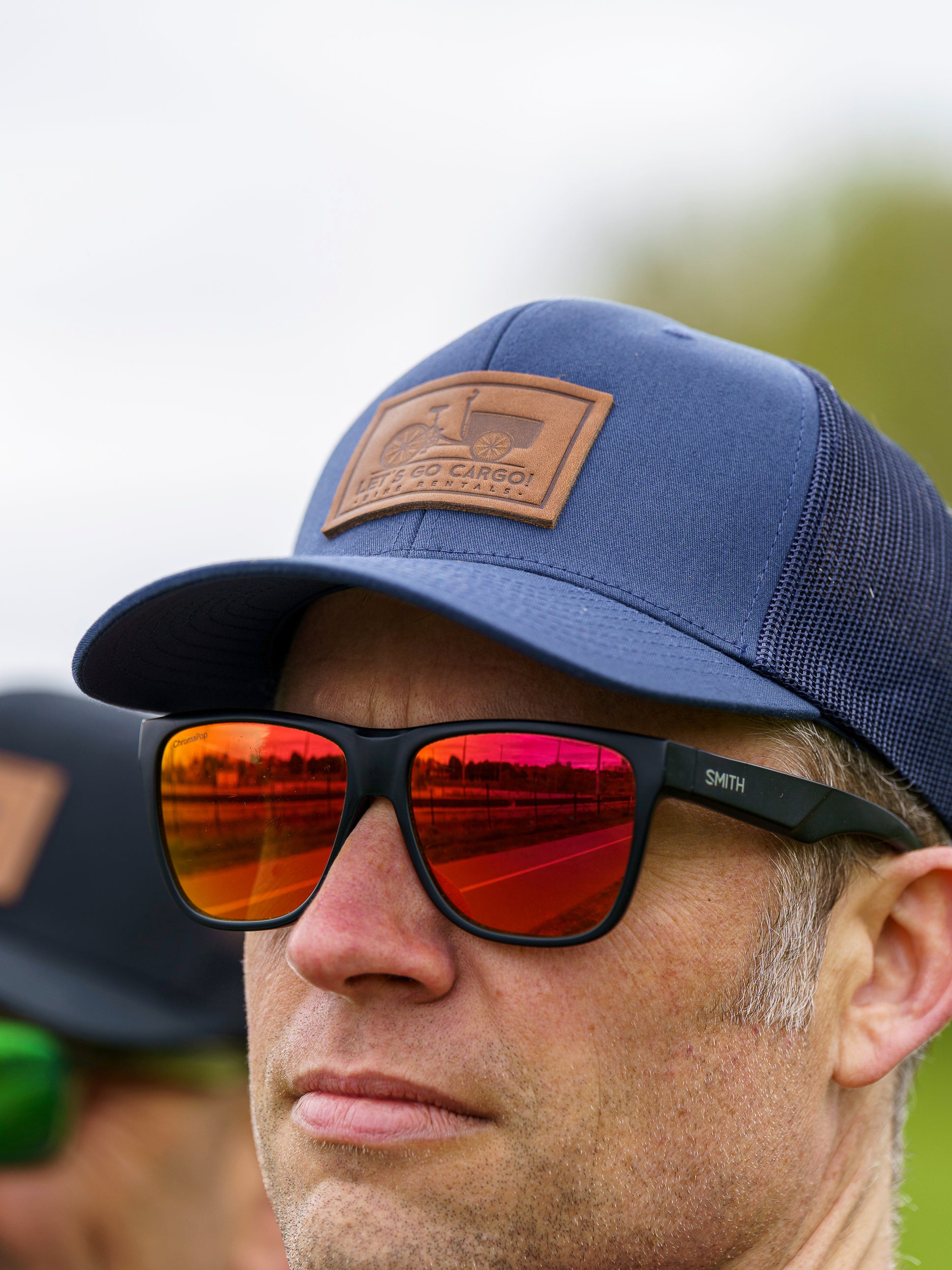 Person wearing a blue cap with a logo and reflective sunglasses outdoors