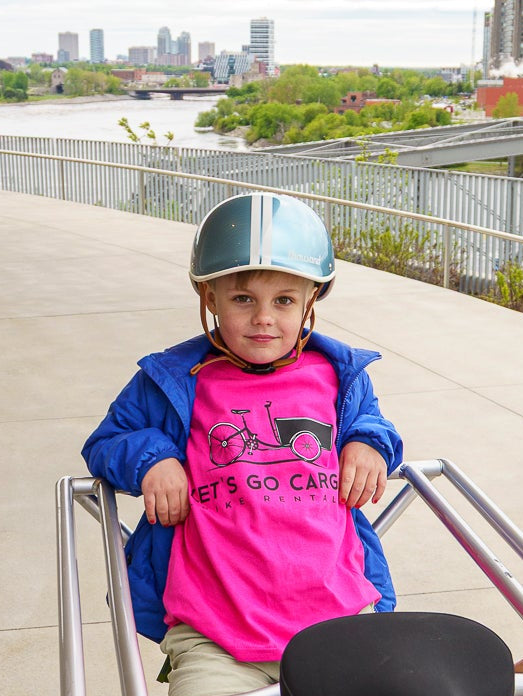 Child on a cargo bike wearing a helmet and watermelon T-shirt.
